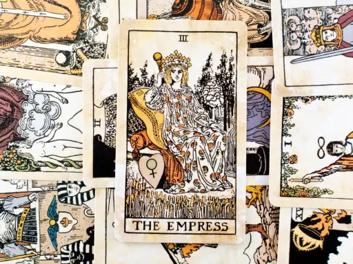 Karta Tarota "The Empress" z koroną i berłem, siedząca na tronie, otoczona innymi kartami.