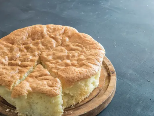 Un gâteau raté, un peu affaissé, sur une planche en bois. Sa texture est spongieuse et sa croûte dorée.
