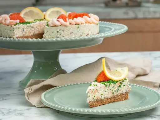 En läcker laxtårta på kavring, dekorerad med räkor, rom och citron. En bit serveras på en mintgrön tallrik.
