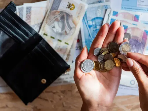 Otwarty portfel, polskie banknoty i monety w dłoni na tle dokumentów.