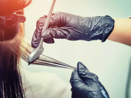 Mani guantate applicano tinta ai capelli. Scopri quanto dura una tinta dal parrucchiere per un colore impeccabile.