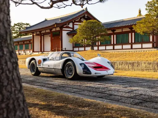 Ein weißer Porsche 966 mit roten Akzenten steht vor einem traditionellen japanischen Gebäude.