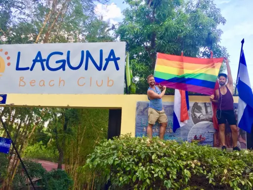 Two men proudly hold a rainbow flag at Laguna Beach Club, celebrating gay pride in Guatemala.