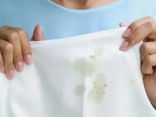 Manos sostienen tela blanca con manchas de grasa. Aprende como quitar la grasa de la ropa fácilmente.
