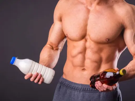 Muskulöser Mann hält Milch und eine Flasche mit bernsteinfarbener Flüssigkeit. Die Frage: Alkohol und Muskelaufbau – eine gute Kombination?