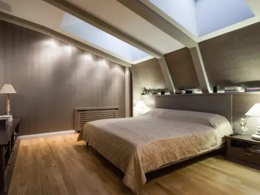 Chambre douillette avec un lit confortable sous une **tête de lit sous pente** et un puits de lumière illuminant la pièce.
