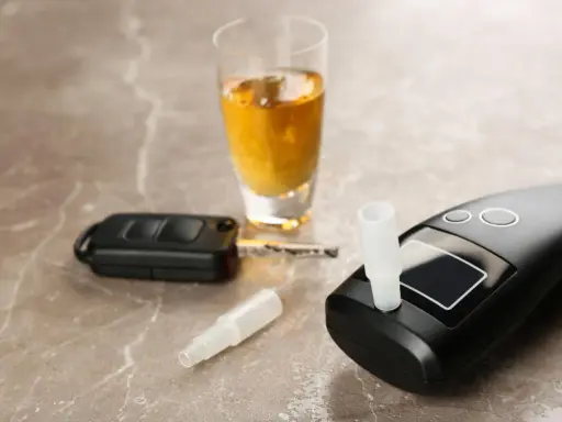 Alkomat, kluczyki samochodowe i kieliszek z alkoholem na marmurowym blacie.