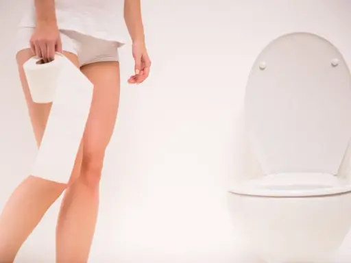 Kobieta z rolką papieru toaletowego obok sedesu. Szuka leków na częste oddawanie moczu w nocy.