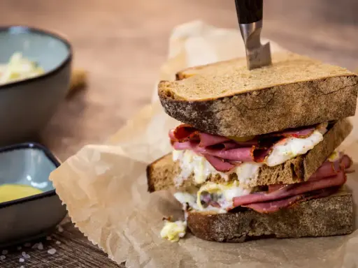 Ein üppiges Pastrami-Sandwich mit Röstbrot, serviert mit Beilagen wie Krautsalat und Senf.