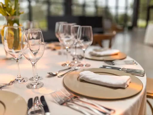 Une table élégamment dressée pour un repas, avec la position des verres à la française. Des assiettes, serviettes et couverts sont prêts.
