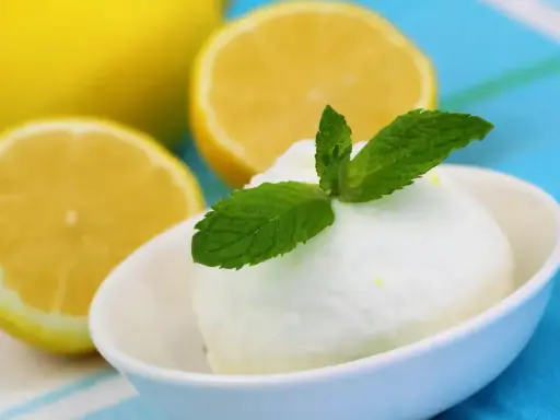 Crème glacée citron rafraîchissante, garnie de menthe fraîche, avec des citrons coupés en arrière-plan.