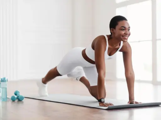 Eine Frau in weißer Sportkleidung macht eine Plank-Übung auf einer Matte. Sie zeigt, was ist gymnastik: Kraft, Ausdauer und Freude an Bewegung.