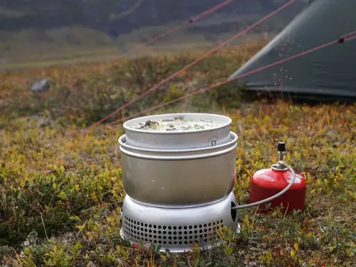 Matlagning på ett esbit kök i fjällen. En kastrull med mat värms upp bredvid ett tält.