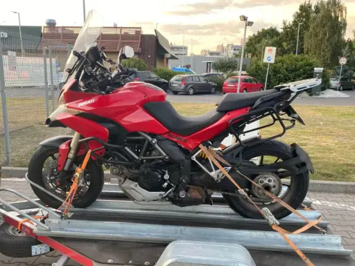 Czerwony Ducati na przyczepie, zabezpieczony pasami do transportu. Gotowy do drogi.