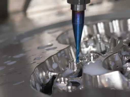 Fresa blu lavora un pezzo metallico, creando dettagli precisi. La cam meccanica è in azione, con liquido refrigerante che schizza.