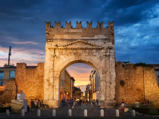 Arco d'Augusto a Rimini al tramonto, con il cielo drammatico e la folla che passeggia. Un'icona della mir fiera Rimini.