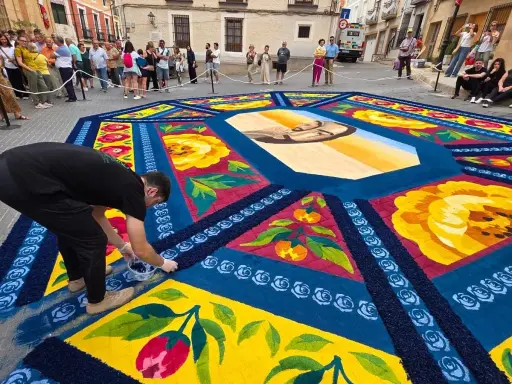 Un hombre finaliza una de las alfombras de serrín de Elche de la Sierra, con un retrato central y motivos florales y frutales.