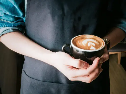 Barista hält eine Tasse mit Latte Art, die die perfekte Cortado Zubereitung zeigt.