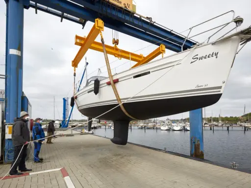 Segelboot "Sweety" wird für das unterwasserschiff reinigen aus dem Wasser gehoben. Männer sichern das Boot mit Seilen.