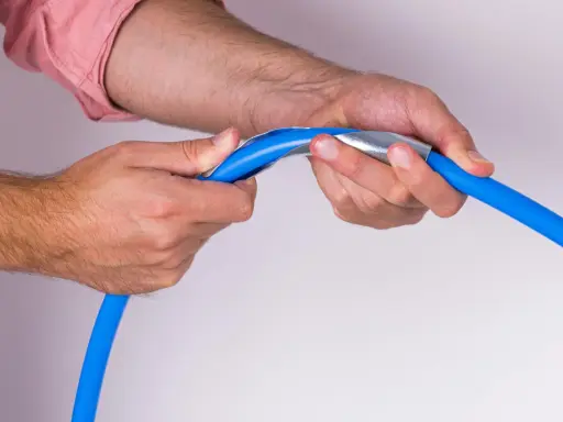 Mains bleues tenant un tuyau bleu avec un outil métallique pour former un coude boule.