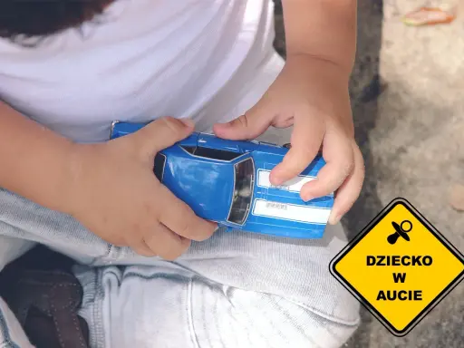 Dziecko bawi się niebieskim autkiem, a obok widnieje żółty znak "Dziecko w aucie", symbolizujący troskę o najbezpieczniejsze foteliki samochodowe.