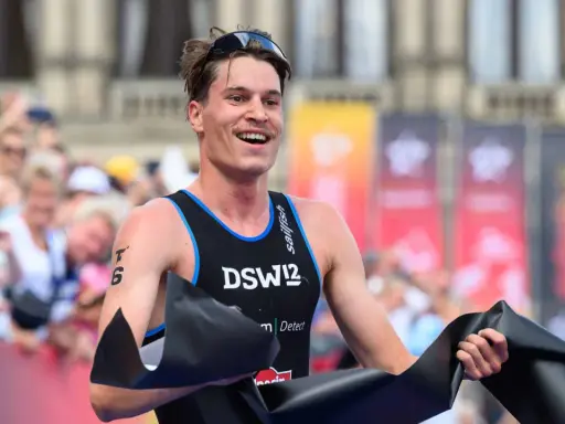 Lächelnder Athlet durchbricht die Ziellinie beim Triathlon Sprint, jubelnd mit schwarzem Band.