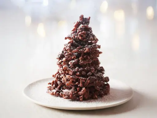 Un sapin chocolat mikado, saupoudré de sucre glace, sur une assiette blanche. Un délice festif !