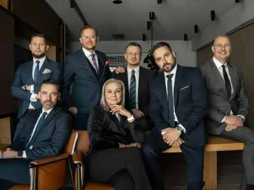 Grupa siedmiu profesjonalistów w garniturach, w tym jedna kobieta, pozuje do zdjęcia.