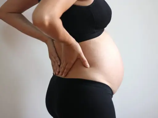 Gravid kvinna med handen på ryggen, upplever ont i ljumsken.
