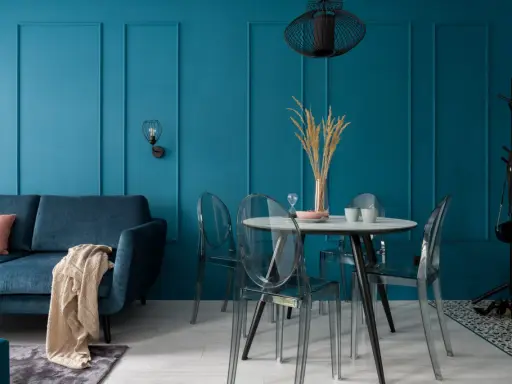 Soggiorno moderno con divano blu, tavolo rotondo con sedie trasparenti e pareti color ottanio.