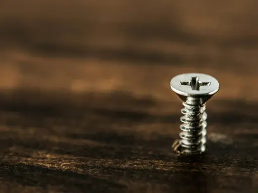 Un tornillo plateado sobre madera oscura. Para sacarlo, gira hacia la izquierda.