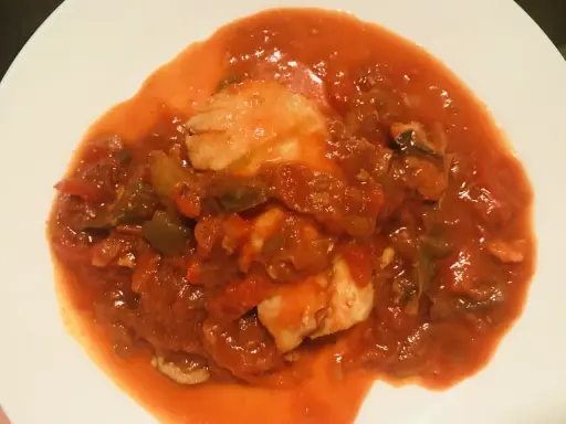 Un plato de urta a la roteña, con trozos de pescado blanco en una salsa roja de tomate y verduras.