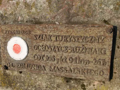 Tabliczka na skale z czerwono-białym kołem i napisem "Główny szlak świętokrzyski im. Edmunda Massalskiego".