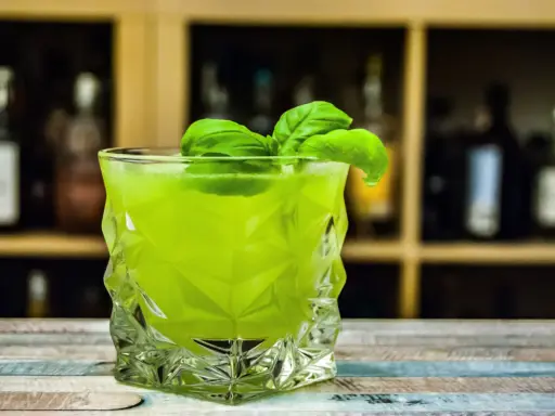Orzeźwiający drink z likierem miętowym, ozdobiony listkami bazylii, w szklance o geometrycznym kształcie.