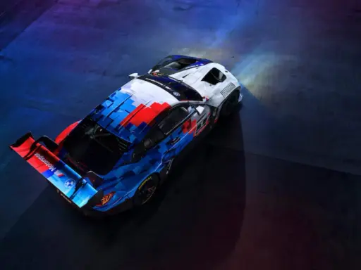 Der BMW M4 GT3 in dynamischer Motorsport-Lackierung steht bereit für die Rennstrecke, beleuchtet von Scheinwerfern.