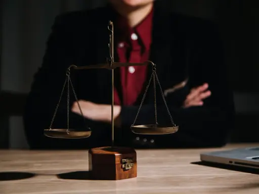 Bilancia della giustizia su un tavolo di legno, con una persona in giacca e camicia rossa sullo sfondo. Le ultime notizie sulla legge Pinto sono in arrivo.
