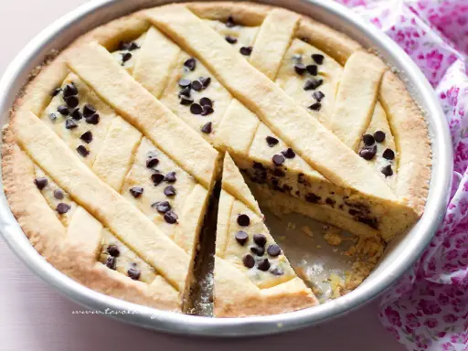 Deliziosa torta ricotta e cioccolato con decorazione a griglia e gocce di cioccolato. Una fetta è stata tolta, rivelando il ripieno cremoso.