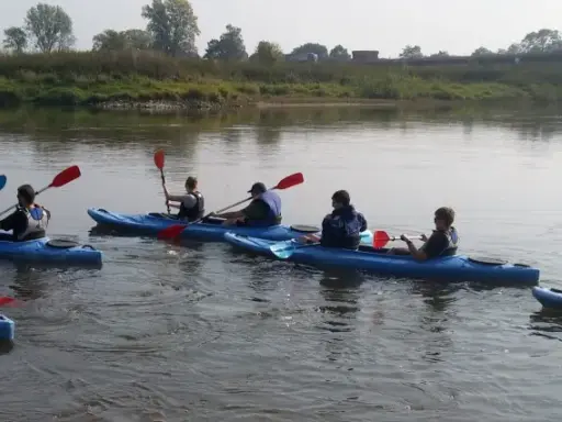 Grupa osób na kajakach płynie po Odrze. W tle widoczny most i zielone brzegi rzeki.