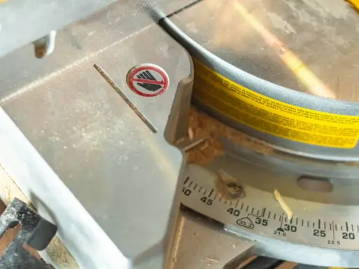 Detalle de una sierra ingletadora con marcas de ángulo para saber como medir para cortar a inglete. Se ve serrín y una advertencia de seguridad.
