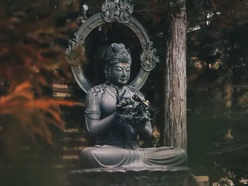 Posąg Buddy w medytacyjnej pozie, otoczony drzewami. Symbolizuje cykl życia i śmierci, buddyzm reinkarnacja.