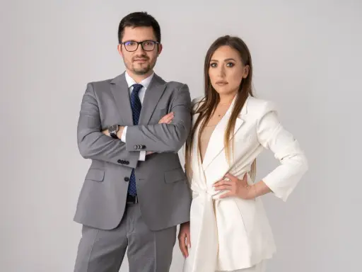 Para prawników w garniturach, mężczyzna w szarym, kobieta w białym, na jasnym tle.