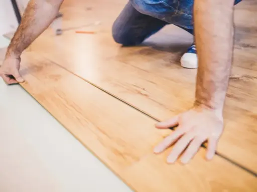 Mann verlegt Laminat. Die Holzoptik der Dielen wird sorgfältig zusammengefügt.