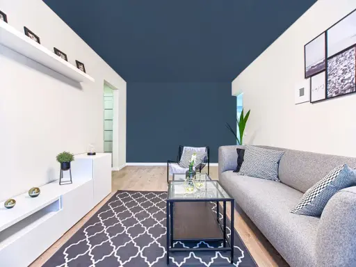 Un salon moderne avec un canapé gris, une table basse en verre et un tapis à motifs. Le plafond bleu foncé donne une impression de profondeur, une astuce pour comment agrandir une pièce.