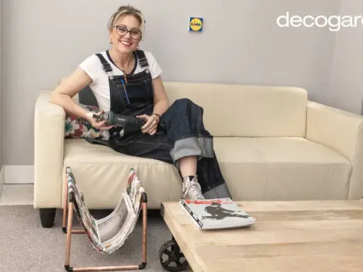 Mujer con overol sentada en sofá beige, sosteniendo una herramienta. A su lado, un revistero diy hecho con cobre y tela.