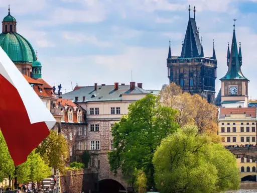 Flaga Czech powiewa nad Pragą, ukazując ciekawe fakty o Czechach. W tle widać Most Karola i wieże.