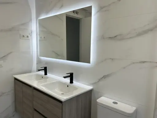 Moderno lavabo doble con grifería negra y espejo iluminado. Una solución ideal para reformar baño sin obras, con un toque de elegancia.
