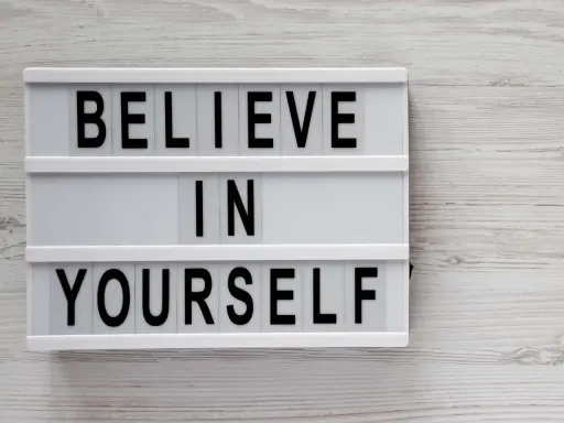 Biała tablica z czarnymi literami: "BELIEVE IN YOURSELF". To przesłanie inspiruje do nastawienia na rozwój i wiary we własne możliwości.