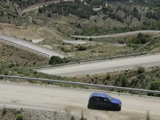 Coche azul en carretera de montaña con curvas pronunciadas. Podría recibir una multa por circular por pista forestal.