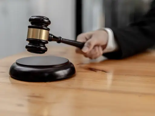 Mano che impugna un martelletto da giudice, pronto a battere sul ceppo. Il suo significato, il g.u.p., è un momento cruciale.