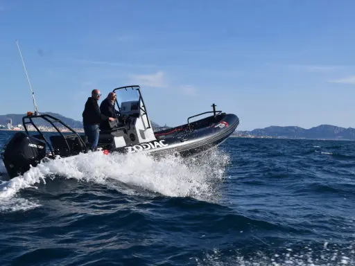 Deux hommes en Zodiac effectuent une navigation mer, projetant des embruns sous un ciel bleu.